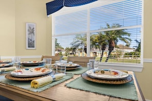 A dining table set with plates, glasses, and placemats, with a view of palm trees through window blinds. - Heated Pool w/ Covered Outdoor Living Near Beach (Marco Island)