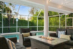 An outdoor patio area with a pool, wicker furniture, and a fire feature. - Heated Pool w/ Covered Outdoor Living Near Beach (Marco Island)