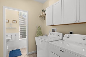 A laundry room with a white washing machine, a dryer, and a shelf above the dryer. - Heated Pool w/ Covered Outdoor Living Near Beach (Marco Island)