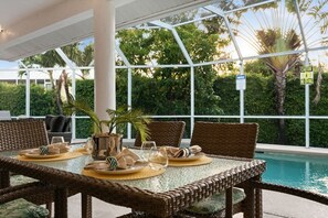 An indoor pool area with wicker furniture and a glass table set for dining.