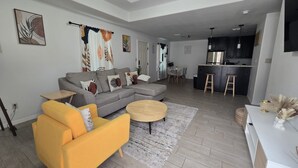 Una sala de estar moderna con un sofá, un sillón, una mesa de centro y una cocina al fondo.