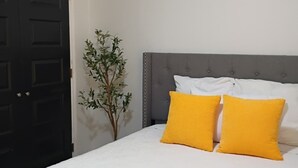 Un dormitorio con una cama, dos almohadas, una planta y una puerta.