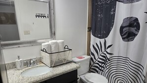 Un baño con lavamanos, inodoro y cortina de ducha con estampado de hojas.