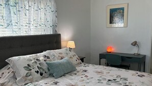 A bedroom with a bed, a desk, a chair, a lamp, and a painting on the wall.