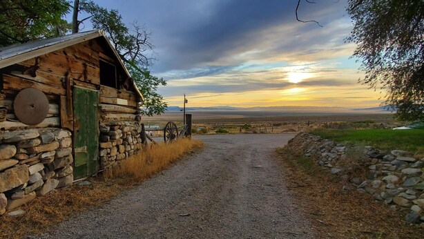 A rustic log cabin with a stone wall, a green door, and a large circular saw blade on the wall.