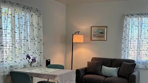 A living room with a sofa, a table with chairs, a floor lamp, and a painting on the wall.