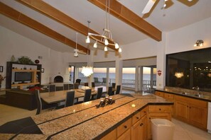 Eine moderne Küche mit Granit Arbeitsplatten, Holzschränken und einer großen Kochinsel. Es gibt einen Essbereich mit Tisch und Stühlen sowie einen Blick auf den Ozean durch große Fenster.