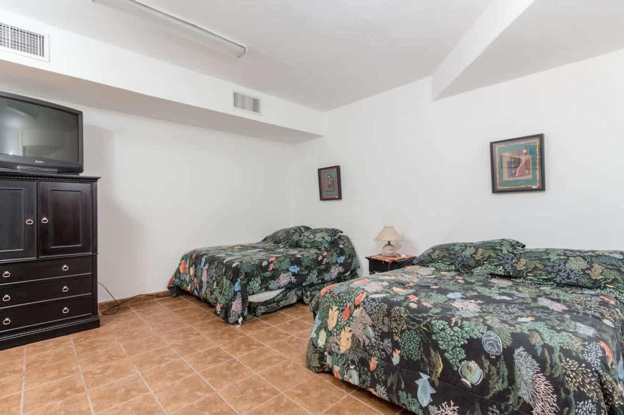 A bedroom with two beds, a TV, a cabinet, and a framed picture on the wall.