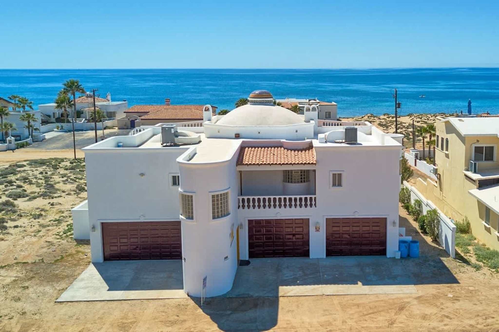 Ein Küstengebäude mit Kuppel, zwei Garagen und einem Balkon mit Blick auf den Strand.