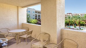 Un balcon avec une table et des chaises, une vue sur un immeuble et un espace piscine agrémenté de palmiers.