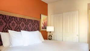 Une chambre d’hôtel avec un lit, une tête de lit ornée d’un motif, un tableau au mur, une lampe et une porte.