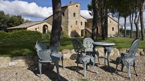 A stone building with a tower, surrounded by trees and a gravel area with metal chairs and a table. - Signorelli (Umbria)