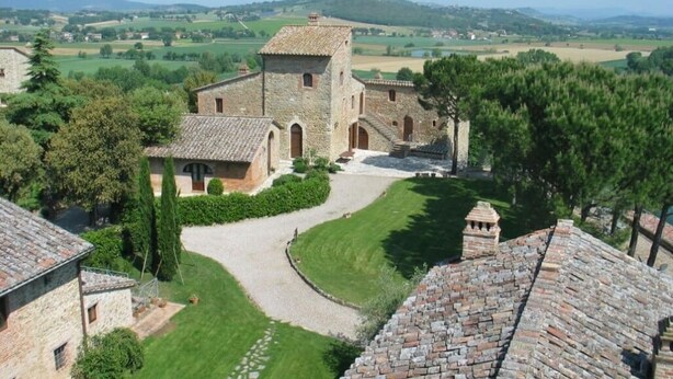A stone building with a central tower, surrounded by a well-maintained lawn and a gravel path. - Signorelli (Umbria)