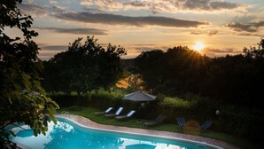A swimming pool with lounge chairs and an umbrella, surrounded by trees and a sunset. - Signorelli (Umbria)