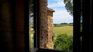 A stone wall through an open window with a view of a green field and trees. - Signorelli (Umbria)
