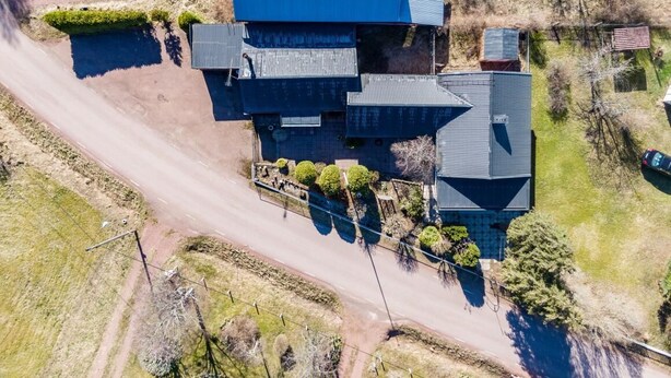 A large, multi-story building with a prominent blue roof, surrounded by a dirt road and sparse vegetation. - Sandmo Holiday Home 11 (Ålands landsbygd)