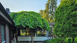 A brick-paved courtyard with a covered seating area, surrounded by lush greenery and a variety of plants. - Sandmo Holiday Home 11 (Ålands landsbygd)