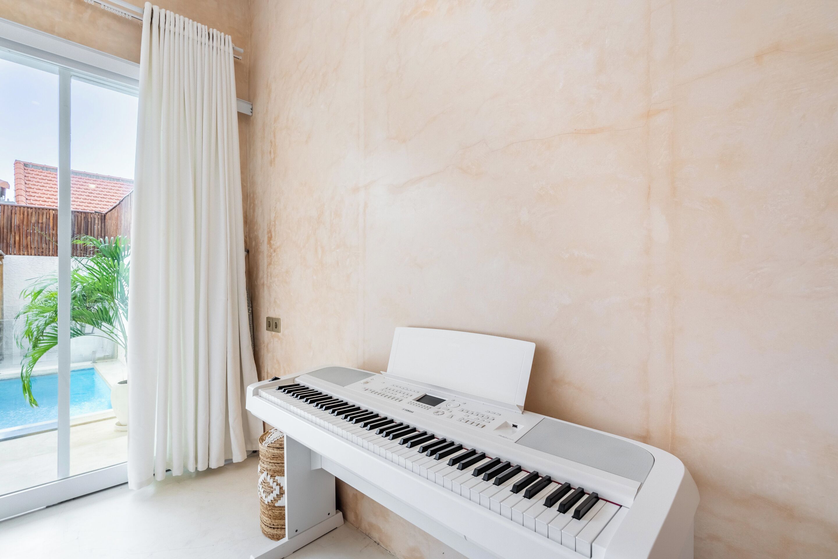 A piano in a room with a large window, a curtain, and a view of a swimming pool.