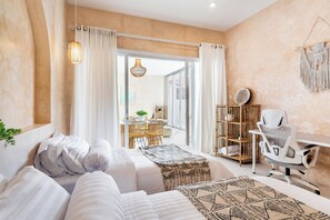 A modern bedroom with a bed, a desk, and a chair. There is a dining area with chairs and a table visible through the glass door. - Sacral Luxury Villa with a private pool (Canggu)