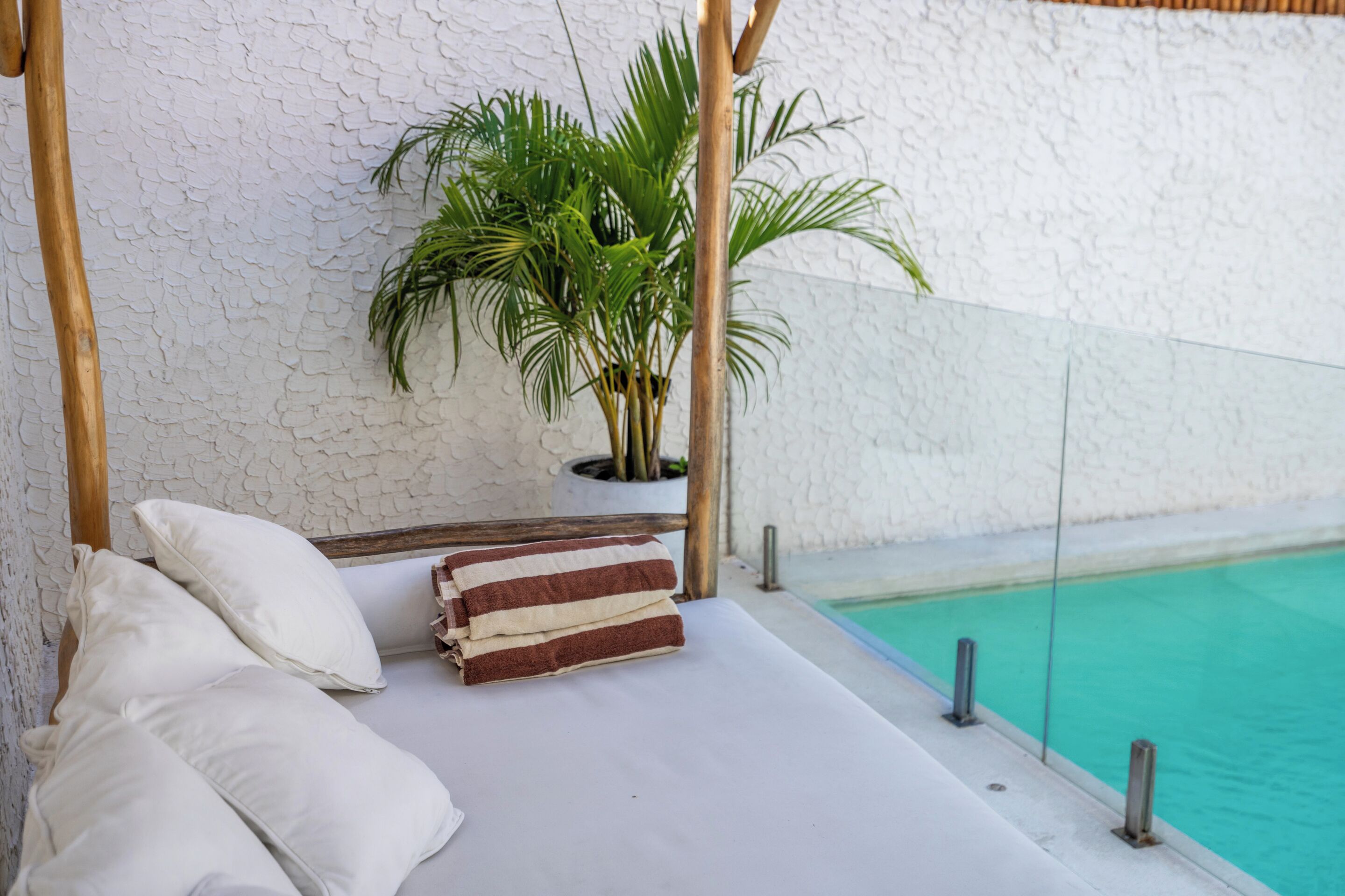 A bed with pillows and a striped towel, a potted plant, and a poolside view.