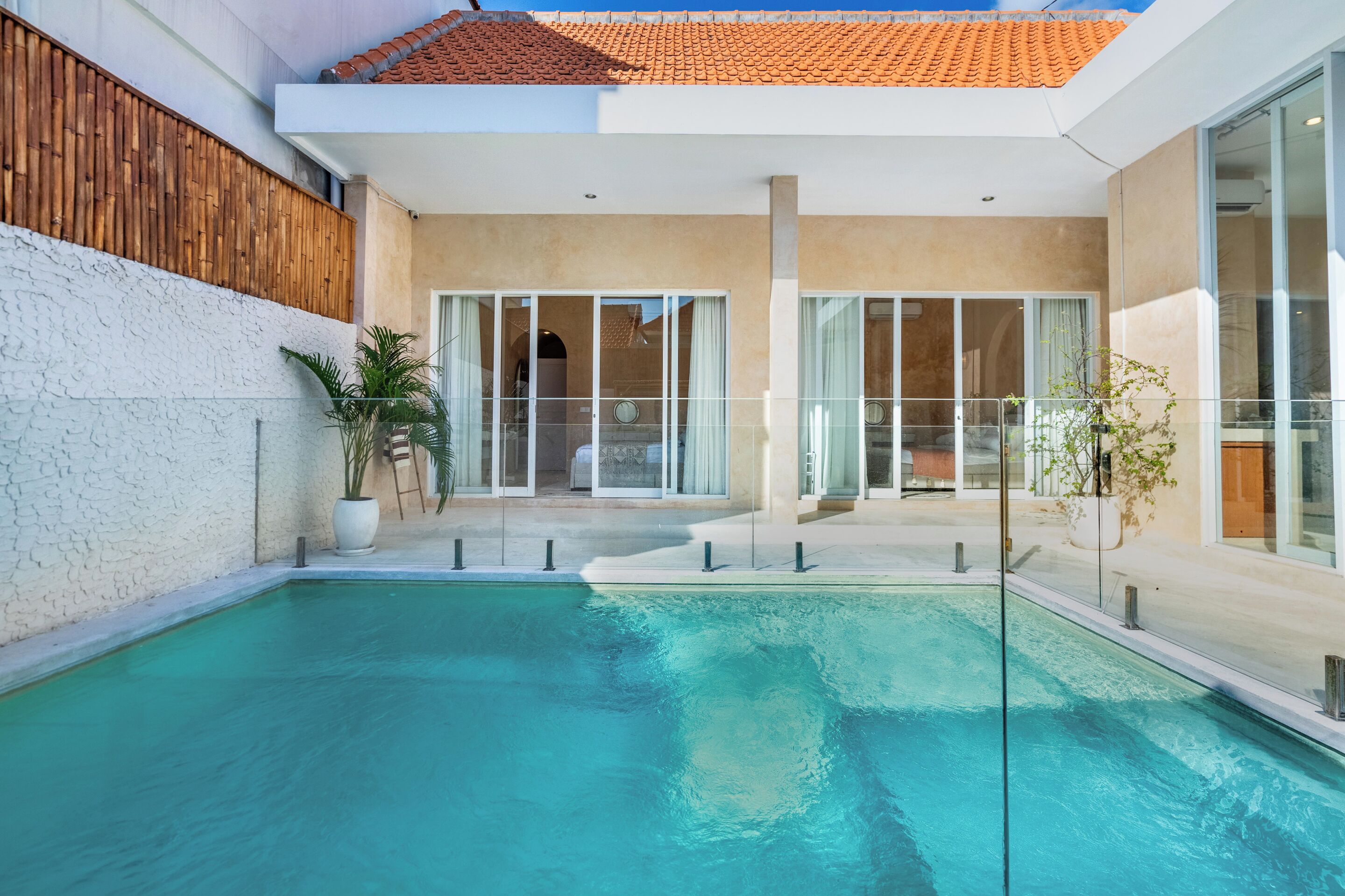 A swimming pool with a wooden deck, glass doors, and a modern building with a tiled roof.