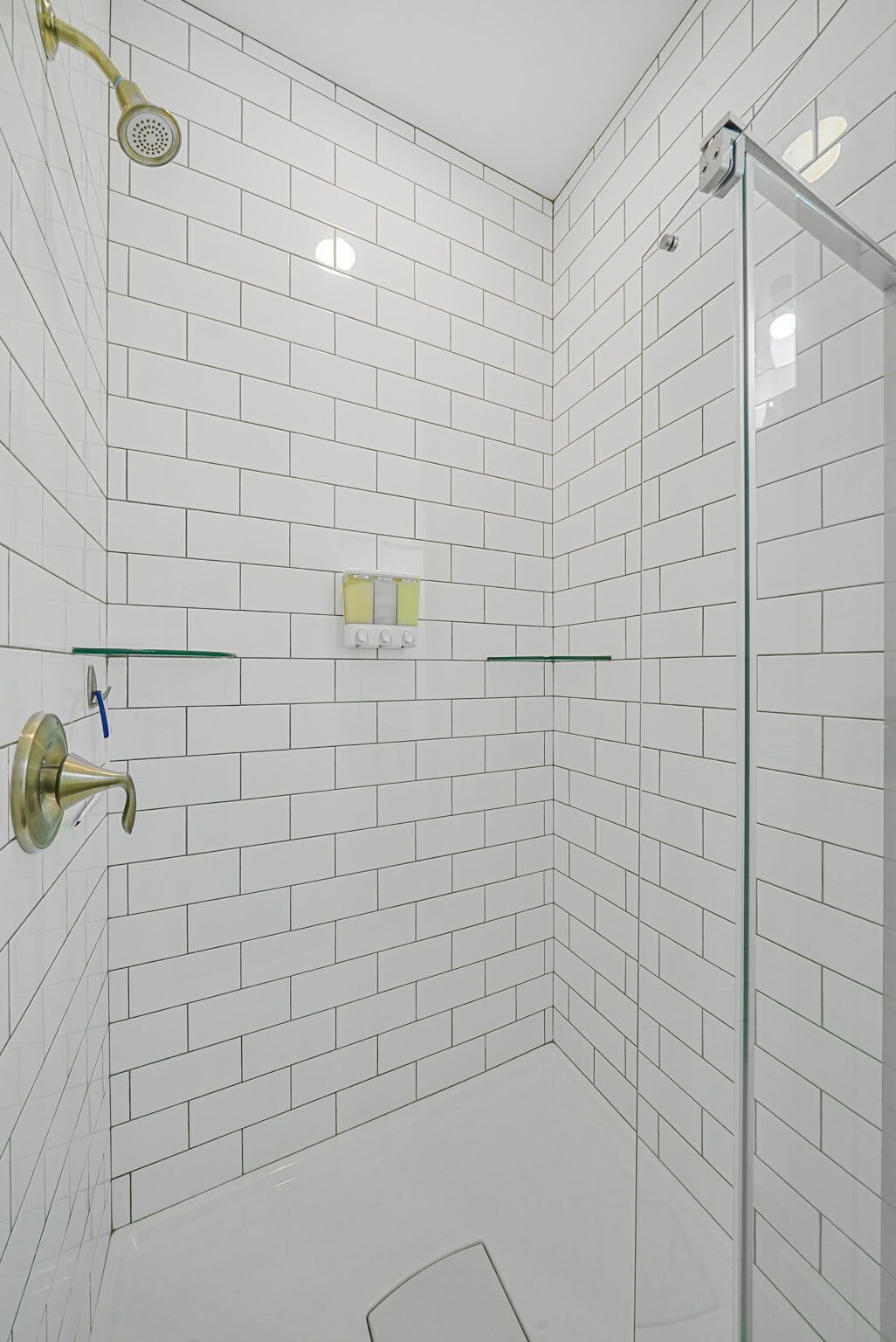 Eine Dusche mit weißen Fliesen, einer Glastür und einer Handbrause.