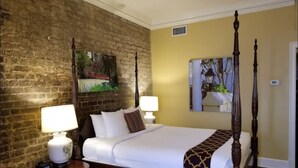 A hotel room with a brick wall, a bed with white linens, two bedside lamps, and a large mirror. - Bluegreen's Lodge Alley Inn: Historic Charm, Modern Comfort, Top Location-Studio (Charleston)