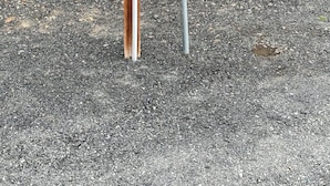 Una cerca de madera, un poste de metal con un grifo y un objeto de metal en el suelo.