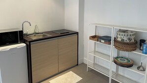 Une cuisine compacte équipée d’un four à micro-ondes, d’un évier et d’une étagère blanche avec des paniers de rangement.