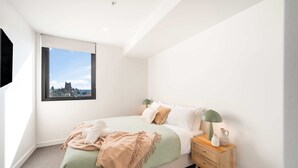 Un dormitorio con cama, mesita de noche, lámpara y ventana con vistas a un castillo.