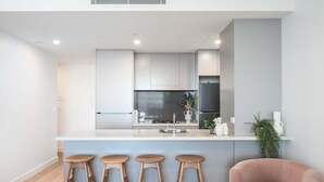 Una cocina moderna con una isla central, taburetes de bar y una silla rosa.