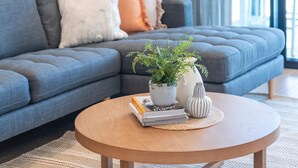 Una sala de estar moderna con un sofá gris, una mesa de centro redonda de madera y una planta verde grande.