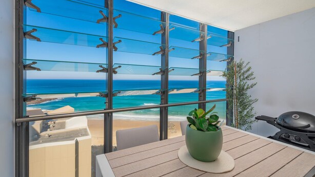 Un balcón con vista a la playa, una planta en maceta y una parrilla.