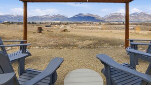 Un espacio al aire libre techado con sillas Adirondack y una pequeña mesa, con vistas a un paisaje montañoso.