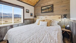 Un dormitorio con una cama grande, paredes de madera, un ventanal con vistas a la montaña y un cuadro en la pared.