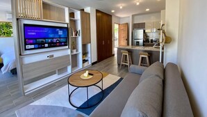 A modern living room with a flat-screen TV, a sofa, a coffee table, and a kitchen area with a bar. - Casa Sisiguaca by Xarm Apartments (Santa Marta)
