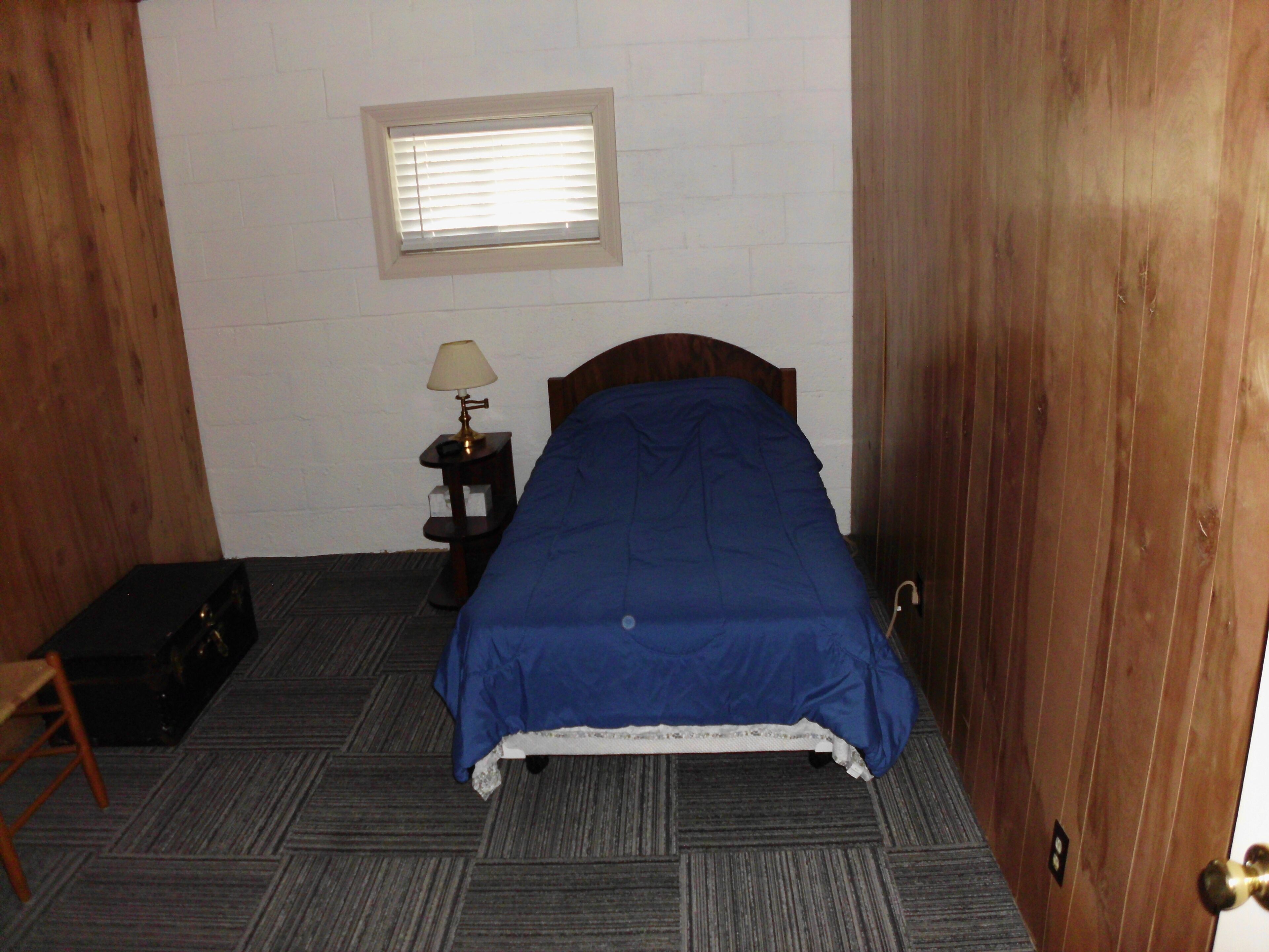 Un dormitorio con una cama, una mesita de noche con lámpara, una ventana y una puerta.
