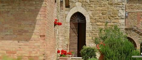 A stone building with an arched entrance, a brick wall, and potted plants.