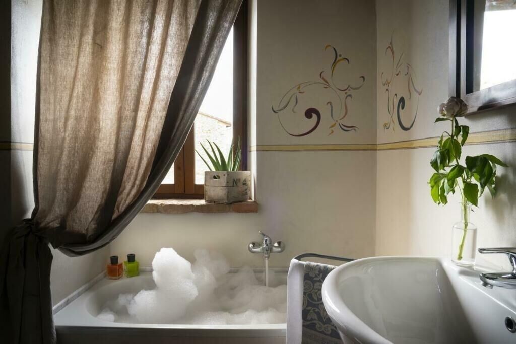 Une salle de bain avec une baignoire remplie de mousse, un lavabo, un miroir et une plante en pot.