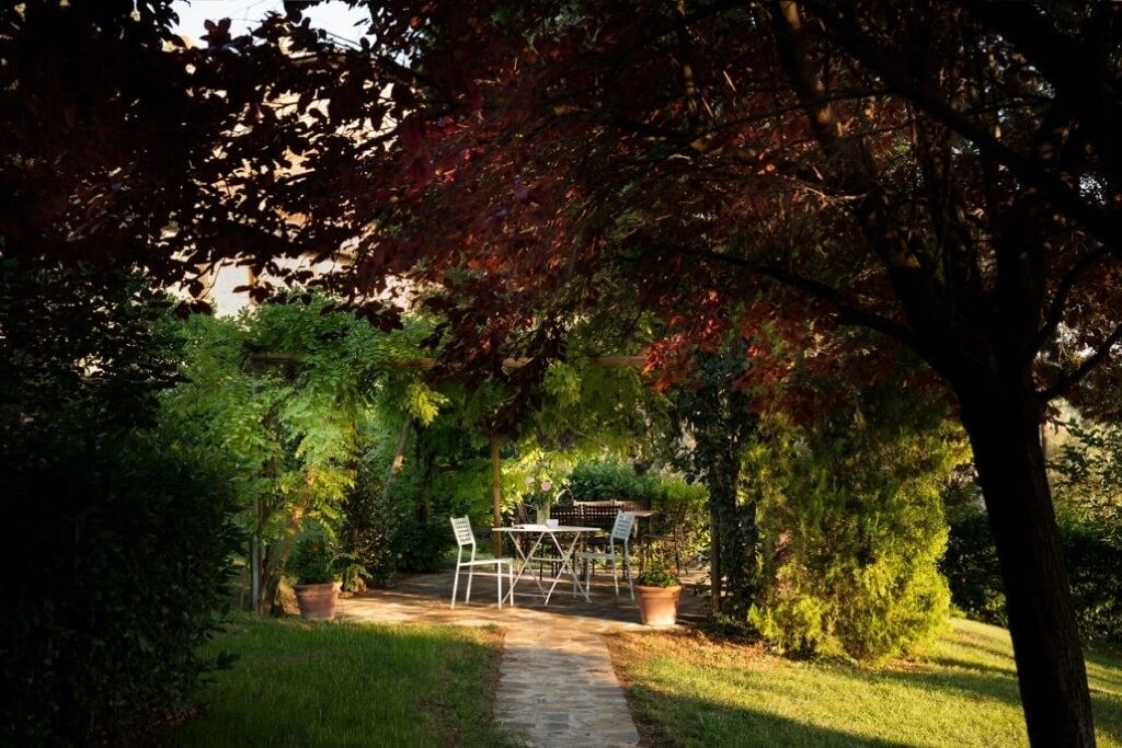 A garden patio with a table and chairs, surrounded by trees and greenery.