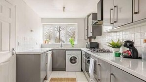Una cocina moderna con lavadora integrada, cafetera y ventana con vistas a árboles.