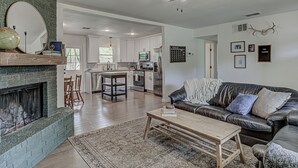 A living room with a fireplace, a leather sofa, a coffee table, and a kitchen in the background. - Awake to Adventure, then Recharge and Relax in Historic Georgetown, Texas! (Georgetown)