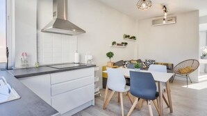 Une cuisine moderne avec des meubles blancs, une hotte en acier inoxydable et un coin repas comprenant une table et des chaises blanches.