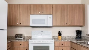 Una cocina con gabinetes de madera, microondas, tostadora, cafetera y estufa.