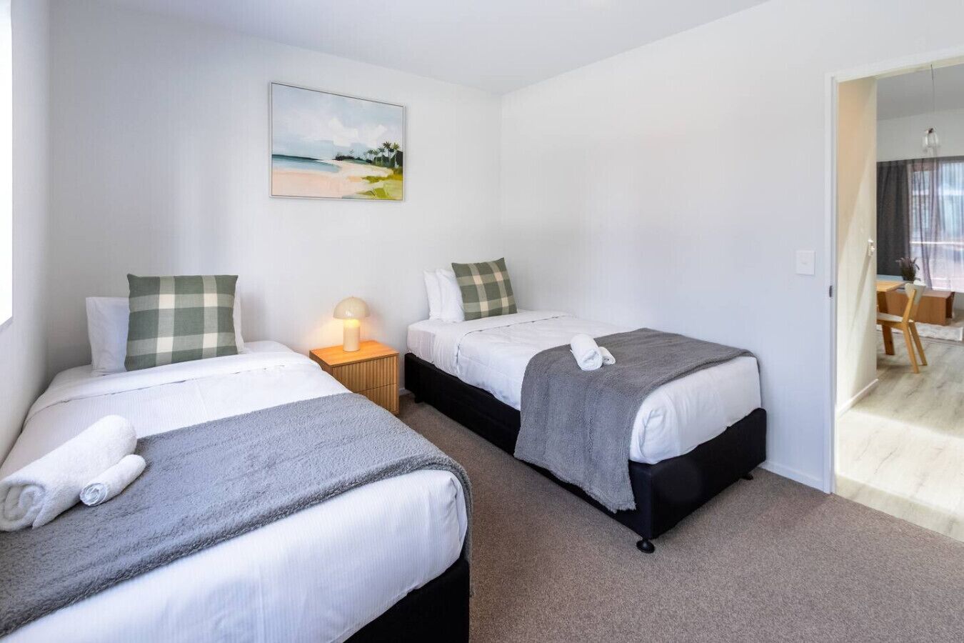 Habitación de hotel con dos camas, una mesita de noche con lámpara, un cuadro en la pared y vistas al exterior.