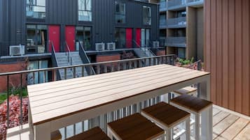 A modern outdoor seating area with a wooden table and benches, overlooking a building with balconies and red accents.
