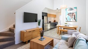 Een modern appartement met een trap, een woonkamer met een bank en salontafel, een eethoek met een tafel en stoelen, een keuken met apparatuur, en een tv aan de muur bevestigd.