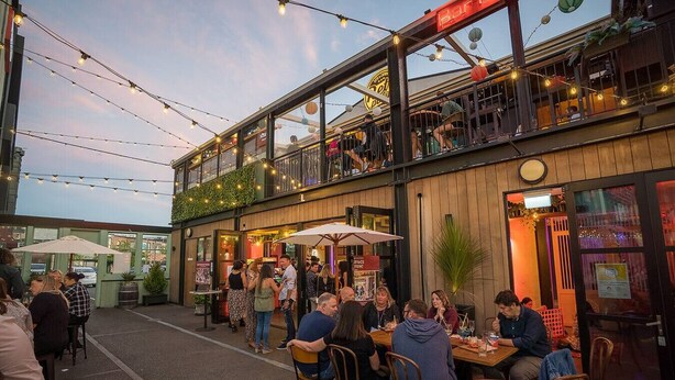 Een terras met tafels en stoelen, een overdekte zithoek en een gebouw met een balkon.