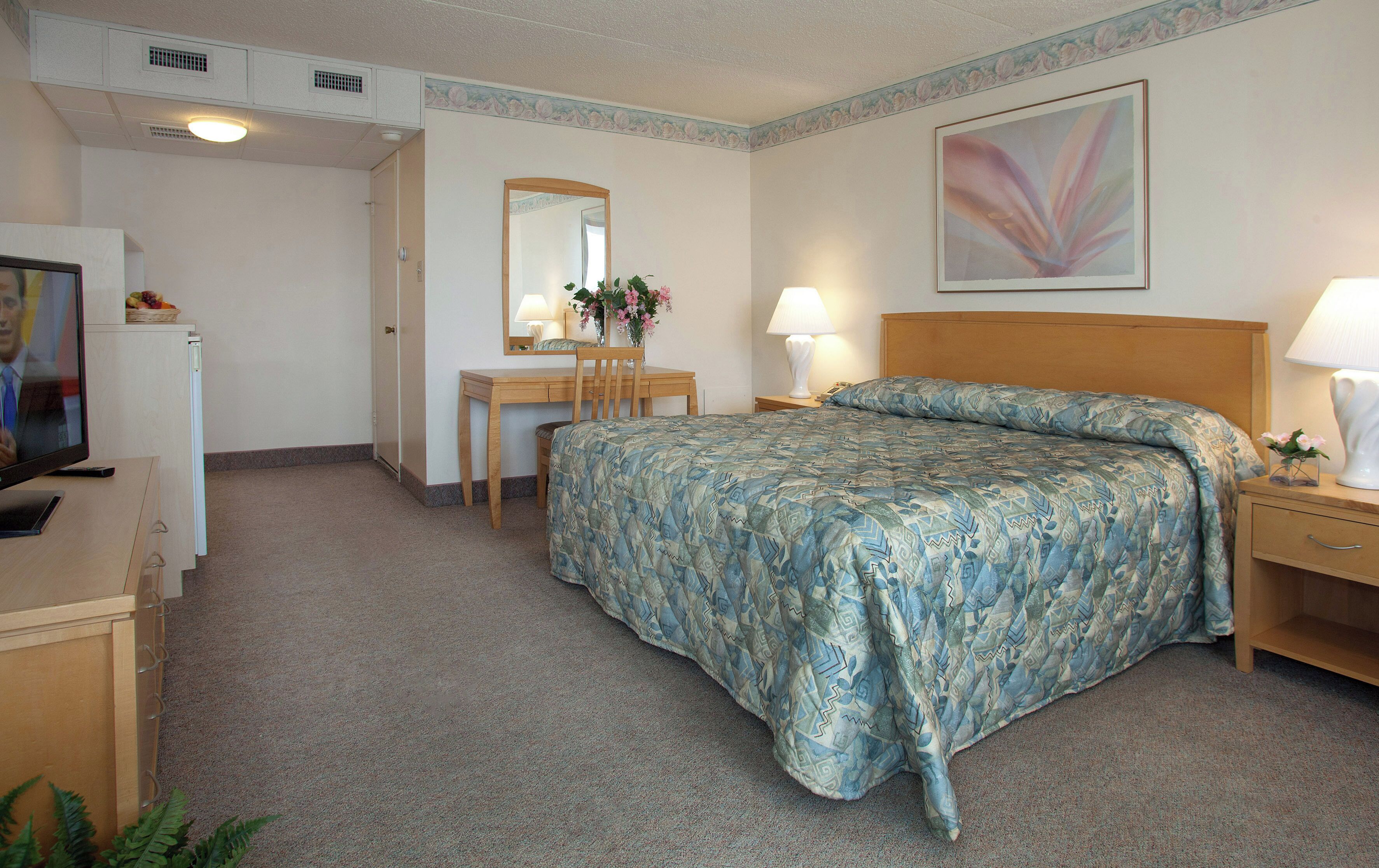 A hotel room with a bed, a desk, a chair, a television, and a lamp.