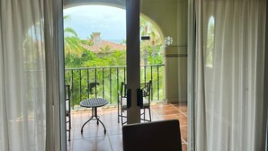 Un balcon avec une table et des chaises, une vue sur la verdure et un bâtiment au loin.